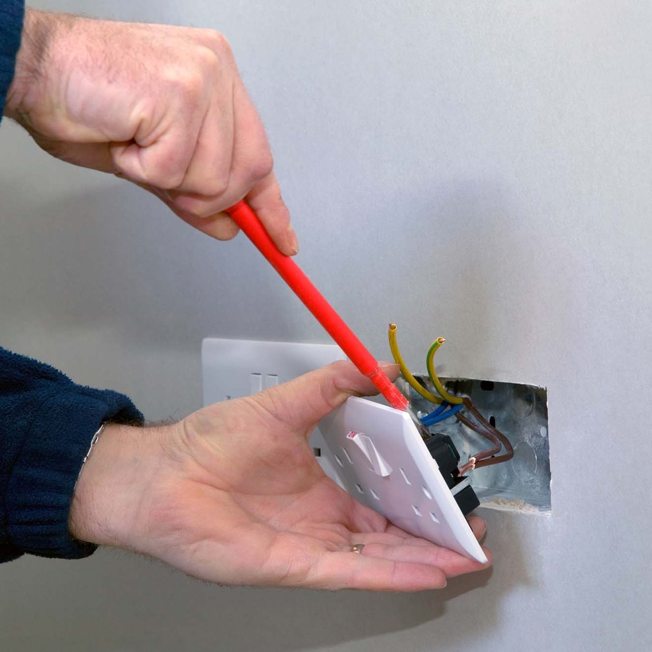 Male electrician cutting wire for socket plug on garage wall